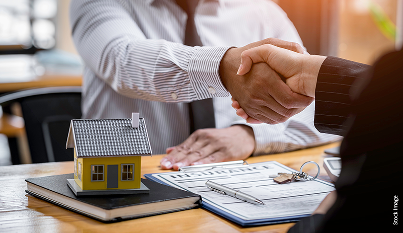 Real estate transaction: handshake agreement with documents, house model, and Zen Home Realty branding on table.